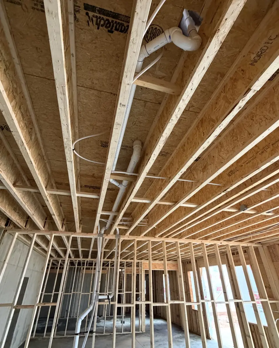 Drain lines run through floor joists in a basement ceiling