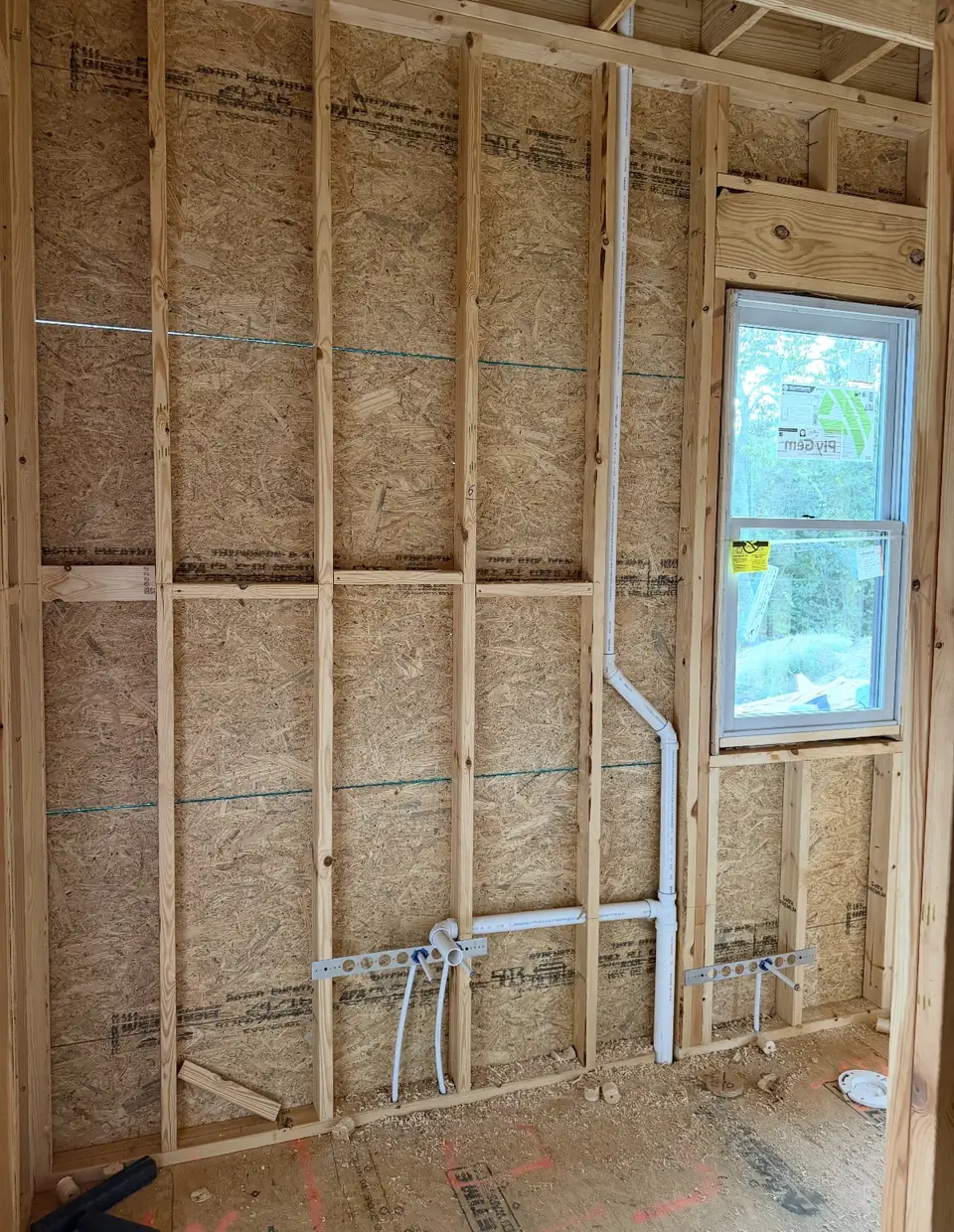 PVC drain and vent rough-in in open studs beside a window